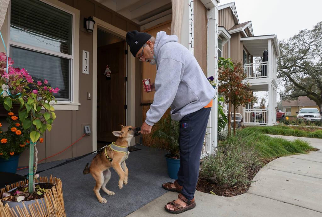 Rafael Castillo, a resident at Windsor Veterans Village, stands with his dog outside of his apartment. He is giving his dog a treat.