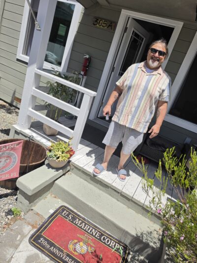 A photo of David as he stands in front of his new house, facing a Marine Corps Veteran front porch mat.